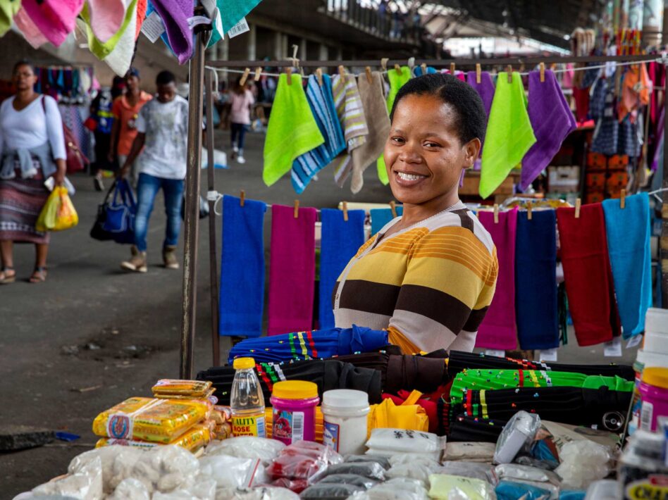 Tina Mteshane smiles at her Brook Street Market stall, surrounded by colorful fabrics.