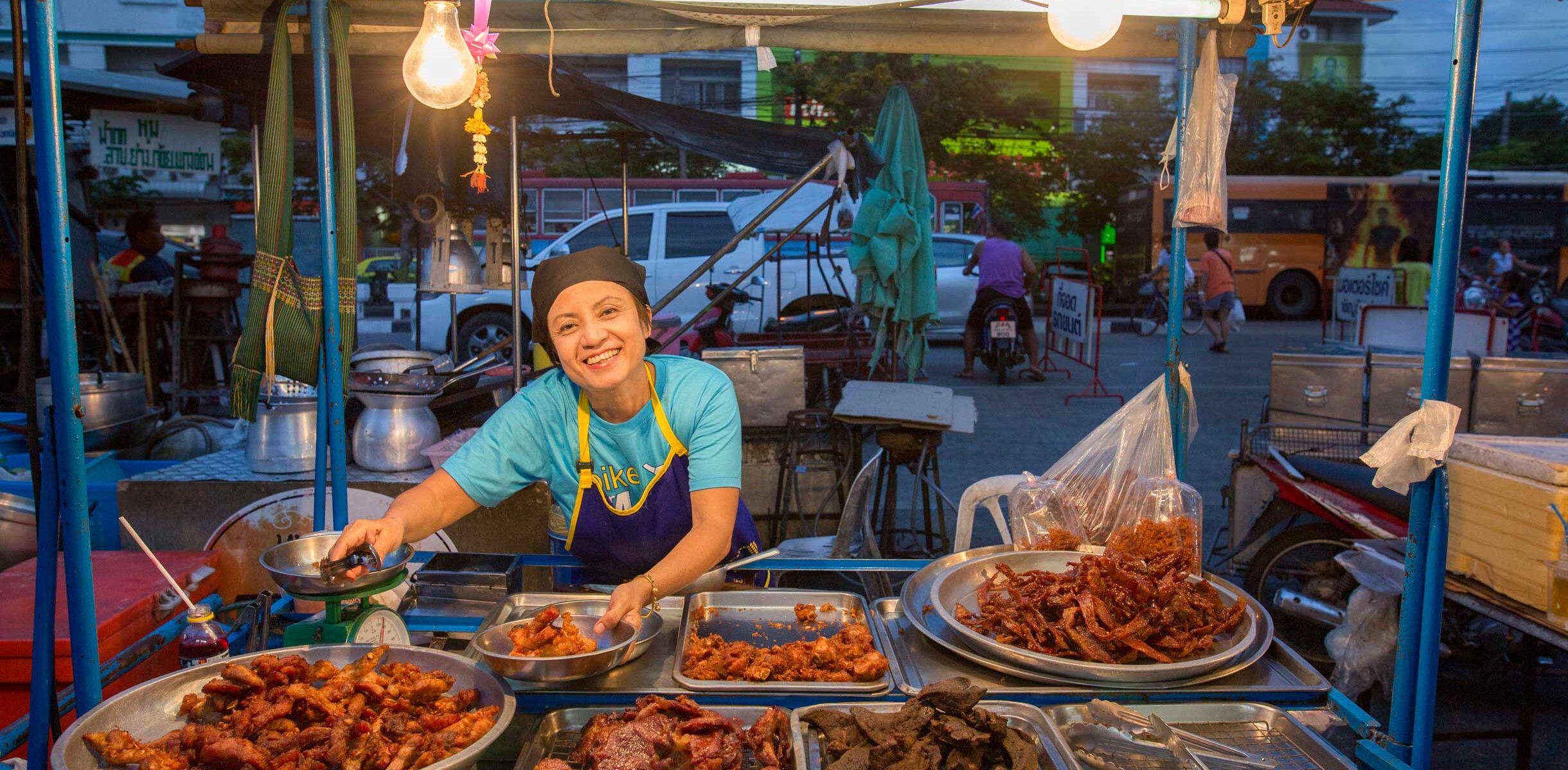 Areerat Chullathip, a street vendor in Bangkok's Economy Square, serves fried food from her stall. As a member of HomeNet Thailand, she works with other vendors to secure vending rights and tackle debt issues through a savings group.