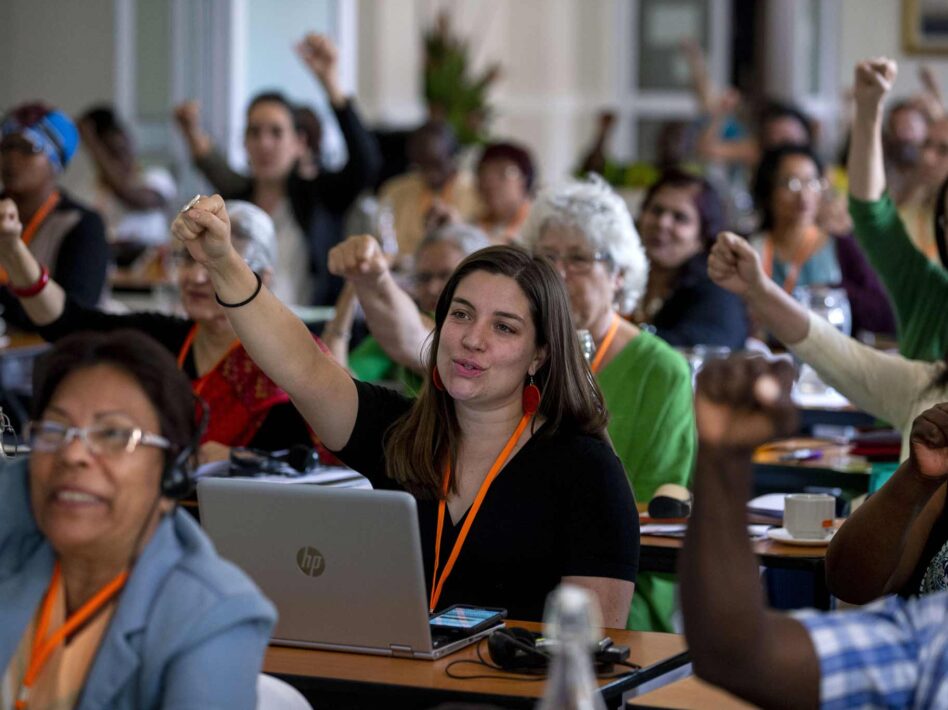 A group of diverse individuals at a conference, raising their fists in solidarity during a session