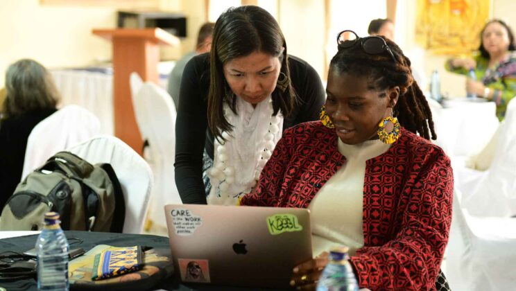 WIEGO team members working together on a laptop during a team retreat in Nairobi, Kenya, collaborating in a supportive environment.