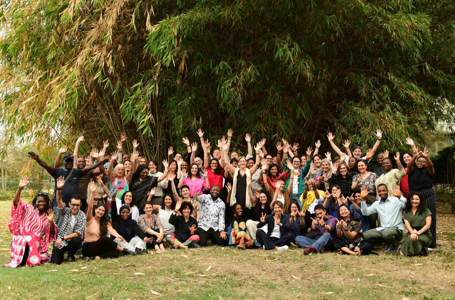 The WIEGO Team poses together outdoors during a team retreat in Nairobi, Kenya, smiling and raising their hands in celebration