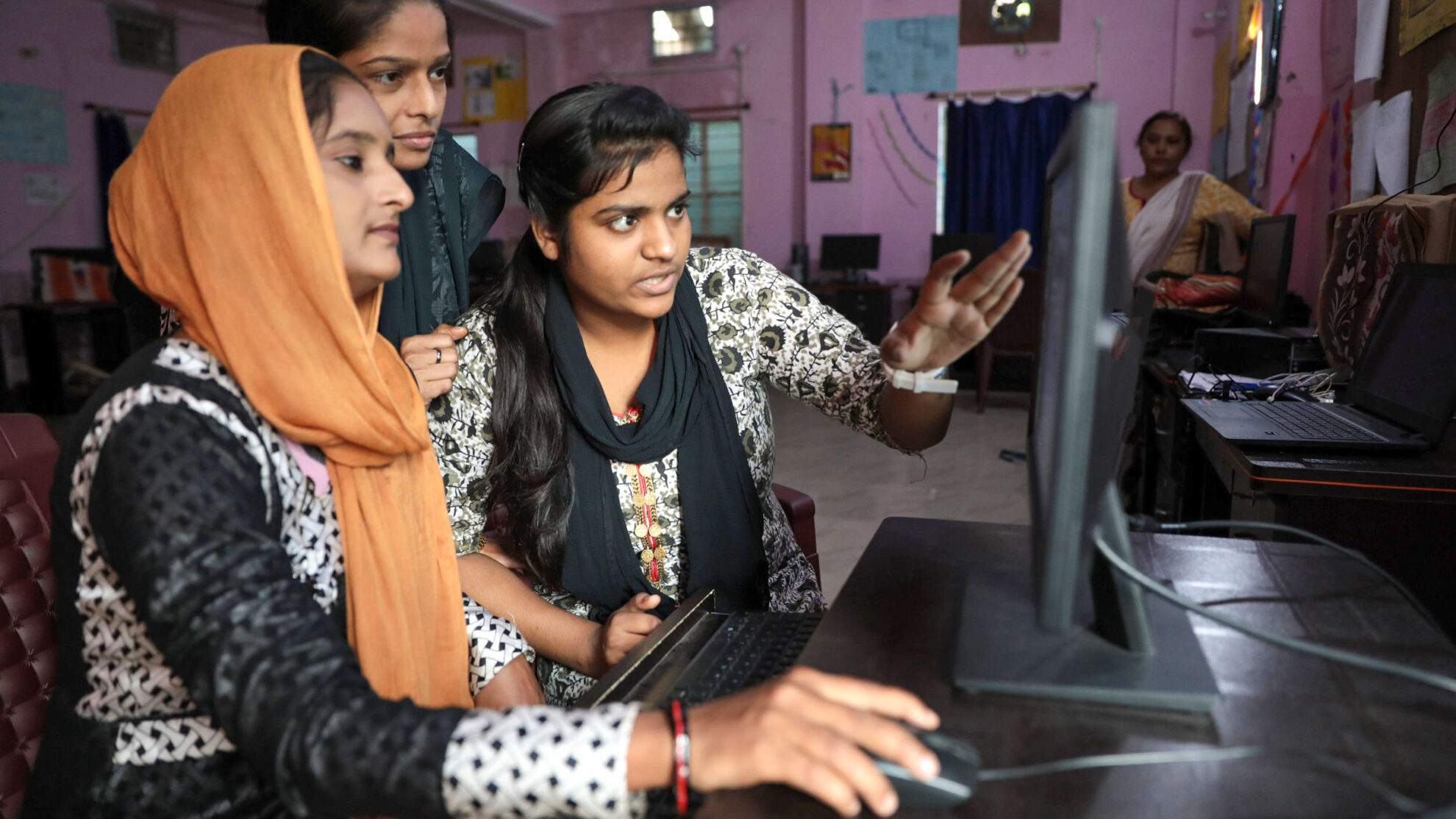 Narmada Ben, an informal worker trained by SEWA and MHT, collaborates with colleagues on a computer as part of her work conducting surveys in her neighborhood slum.