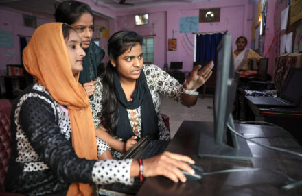 Narmada Ben, an informal worker trained by SEWA and MHT, collaborates with colleagues on a computer as part of her work conducting surveys in her neighborhood slum.