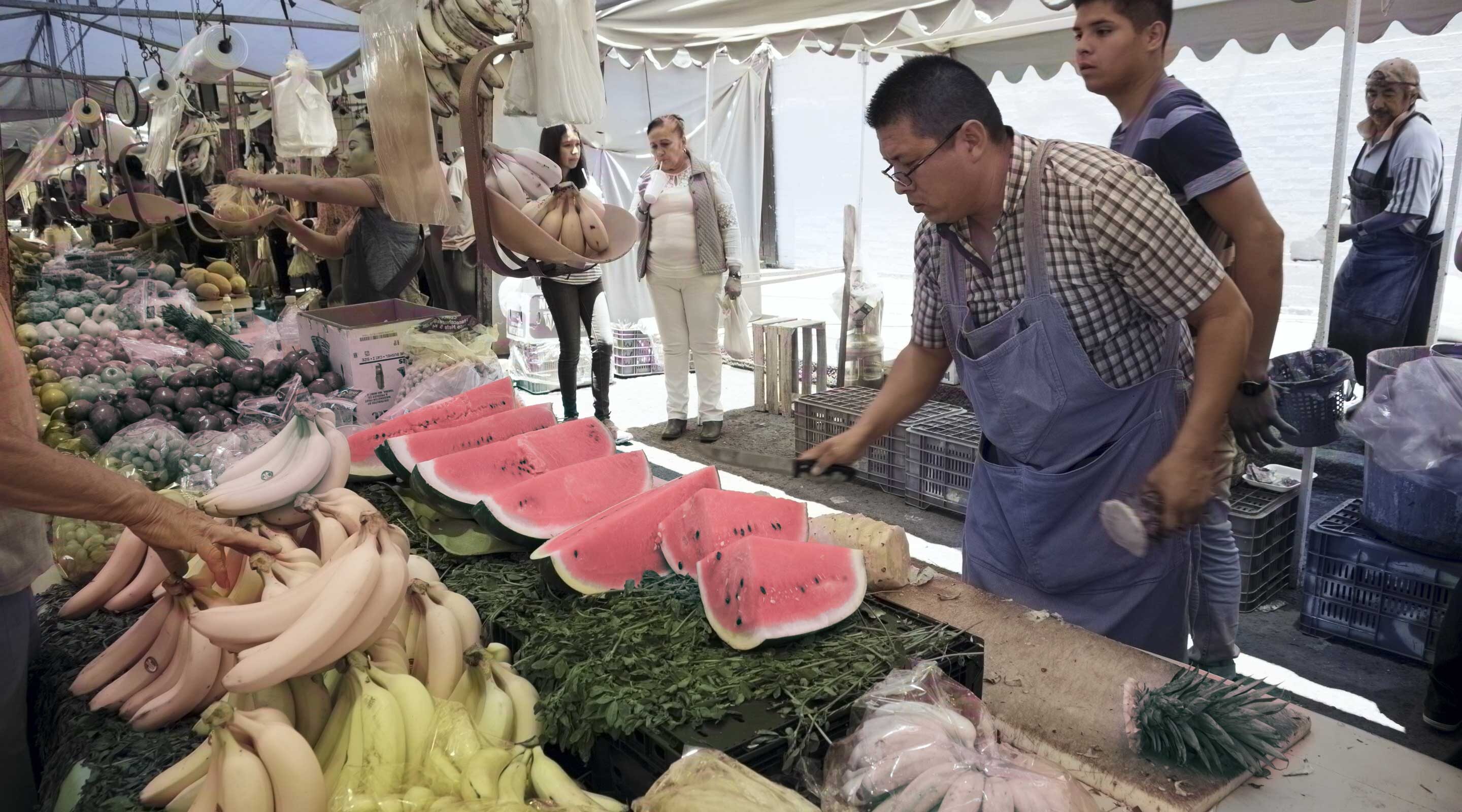 A street vendor in Mexico City prepares fresh watermelon and bananas for customers at a bustling outdoor market