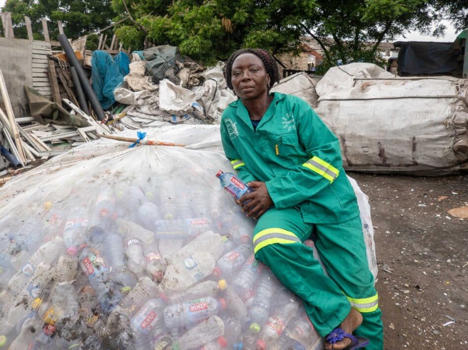 Grace Avemegah con uniforme verde sentada sobre una gran bolsa de botellas de plástico en el vertedero de Kpone.