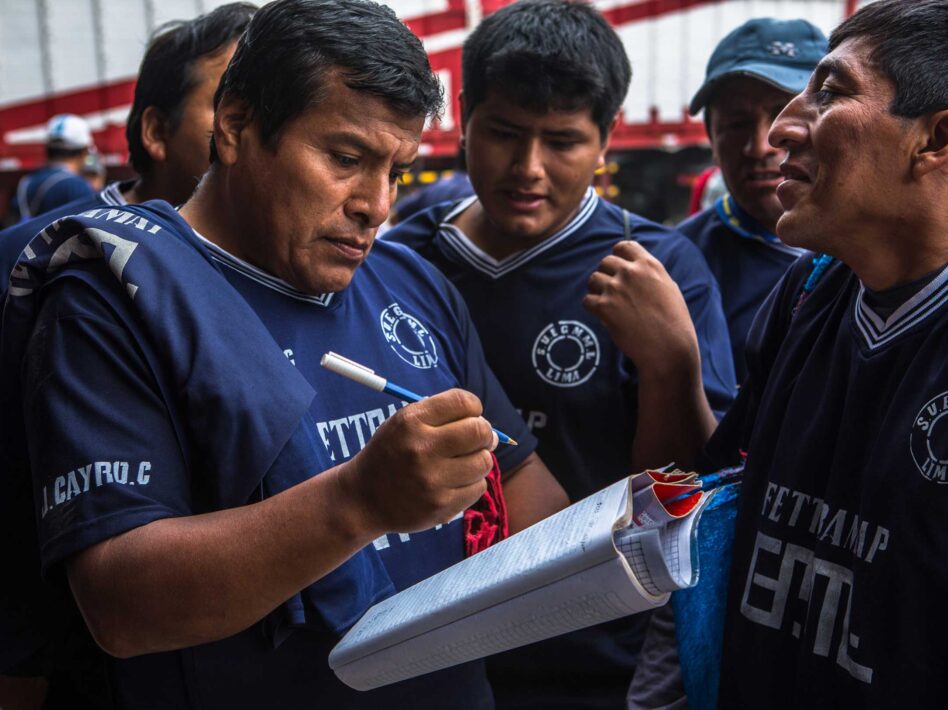 Ricardo Pari Chuhui, a market porter at Lima’s Wholesale Market of Santa Anita, records information while discussing with fellow members of the FETTRAMAP union, which advocates for labor rights despite weak enforcement of occupational health and safety laws