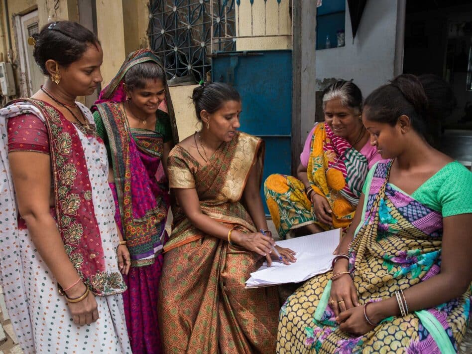 Home-based women workers in Ahmedabad, India, associated with SEWA and MHT, gather outside to discuss neighborhood upkeep and work-related issues, reviewing notes on training and slum upgradation programs.