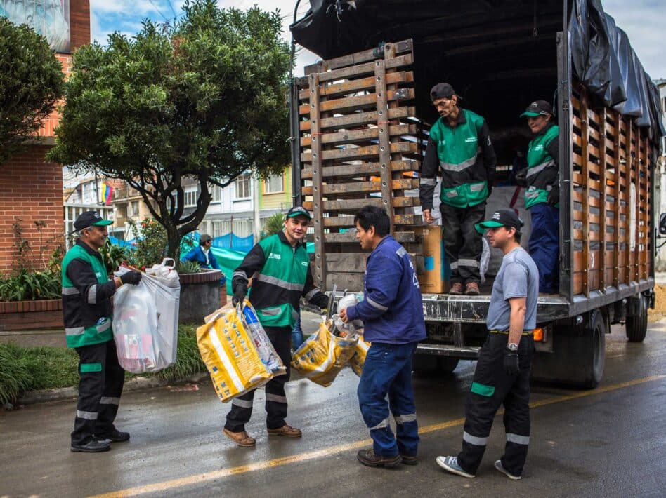 Waste pickers from ARAUS, part of ARB in Bogotá, Colombia, collect recyclables door-to-door in Puente Aranda, educating residents on recycling while loading materials onto a truck.