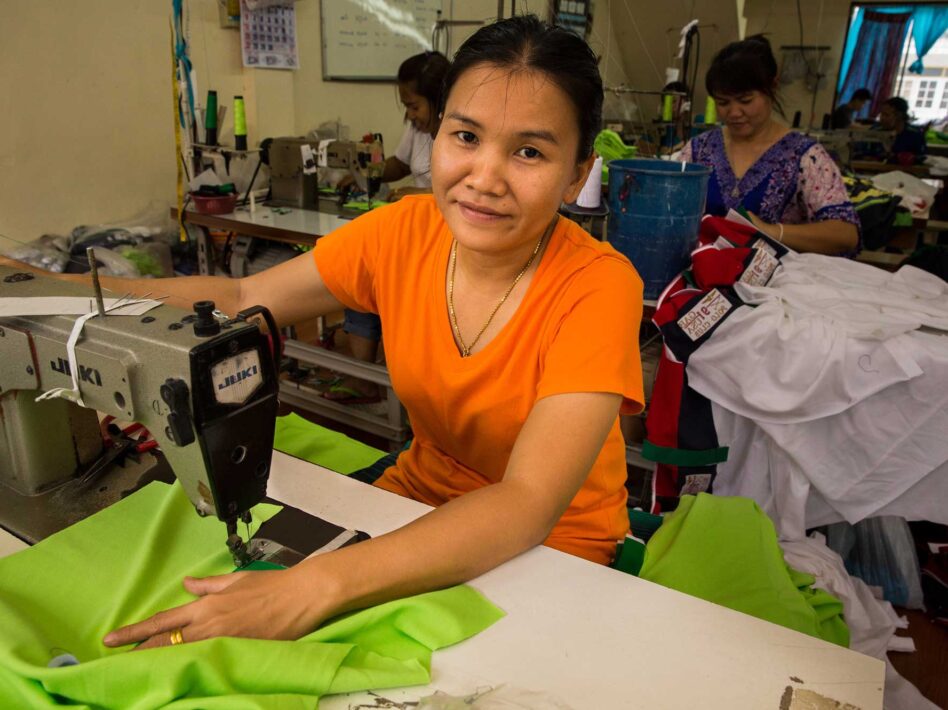 Woman sewing green fabric at a workers'-owned garment factory in Bangkok.