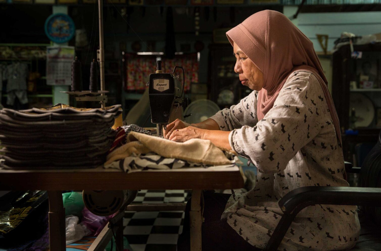 A woman in a hijab sewing garments at home in Bangkok.