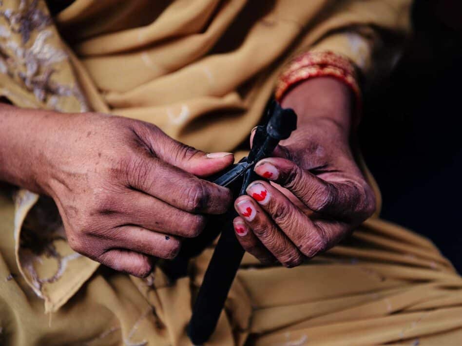 Close-up of a home-based worker’s hands cutting slipper straps in Delhi, India.