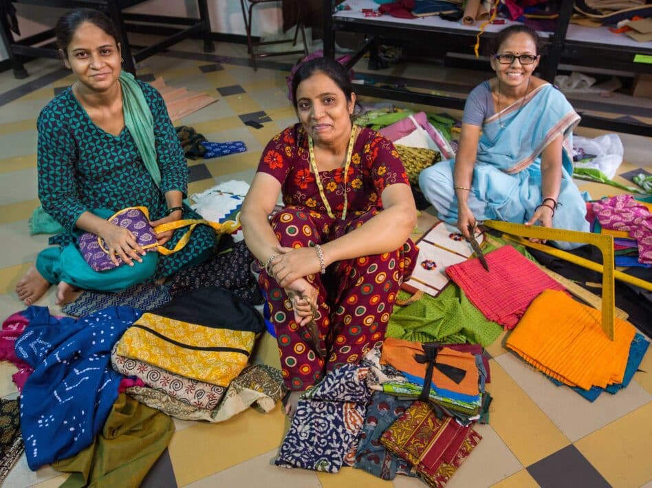 Three Indian women sitting on the floor making handcrafted bags with colorful fabrics.