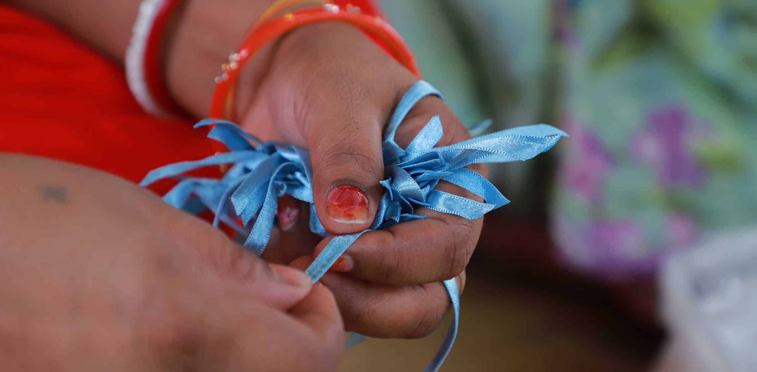 Hands of a worker in India holding blue ribbon decorations.